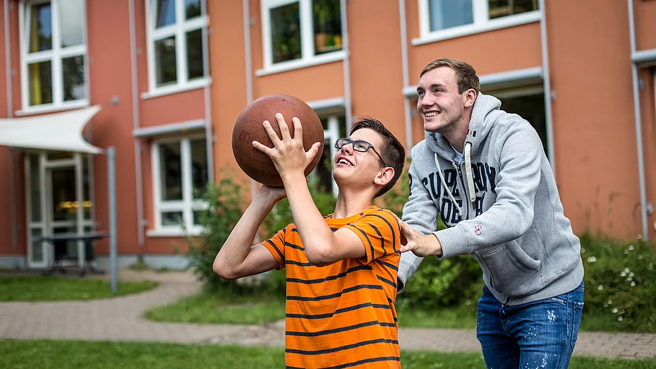 Freiwilliger in der Arbeit mit Kindern Freiwilliger unterstützt Kind beim Basketball